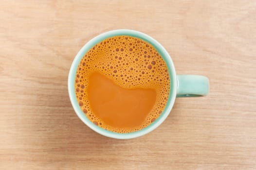 Hot milk tea in a green cup on wooden table background