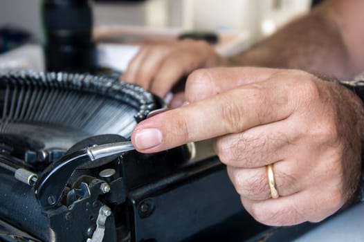 Close-up of male hand operating the carriage return lever at a vintage black typewriter.