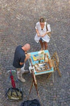 female Holidaymaker in the old town of Malcesine in Italy buys a painted picture from a street artist as a souvenir