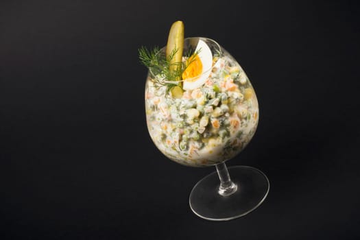 Russian salad served in drinking glass on black background.