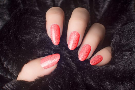 Female hand with glittered red nails is holding black fur, manicure and nail care concept.
