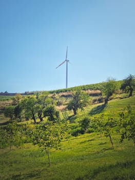 Wind turbine on the top of a hill over the country valley with vineyard and fruit trees. Green energy conservation and environmental concepts