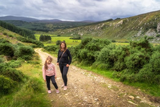 Mother and daughter standing on country road with green mountain valley in background. Family hike in Lough Dan, Wicklow Mountains, Ireland