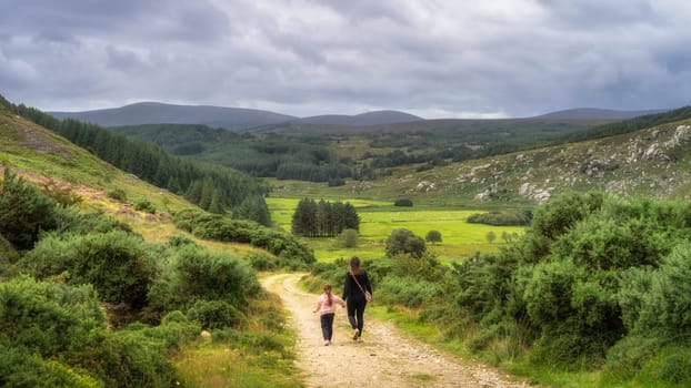 Mother and daughter walking down on country road towards green mountain valley. Family hike in Lough Dan, Wicklow Mountains, Ireland