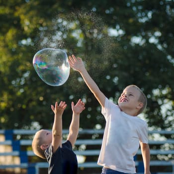 Two little boys are playing with soap bubble outdoors, happy and carefree childhood.