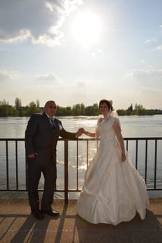 Sremska Mitrovica, Serbia October 10, 2019: the bride and groom hold hands and look forward. The river and the sun are visible in the background.