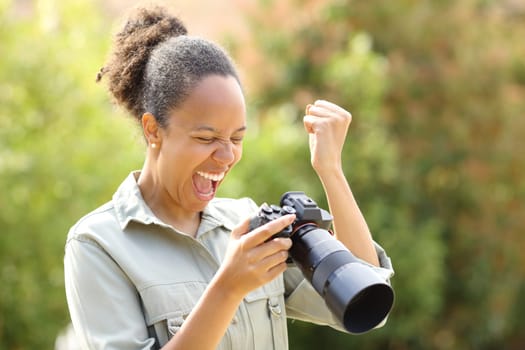 Excited black photographer checking good result standing in a park