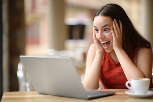 Amazed woman finding good news on laptop sitting in a bar terrace
