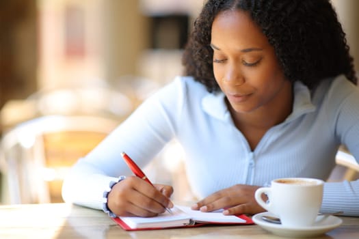 Black woman writing on paper agenda in a bar terrace