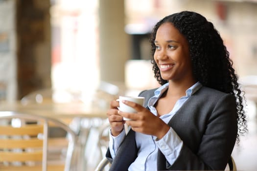 Happy black businesswoman enjoying coffee sitting in a restaurant terrace