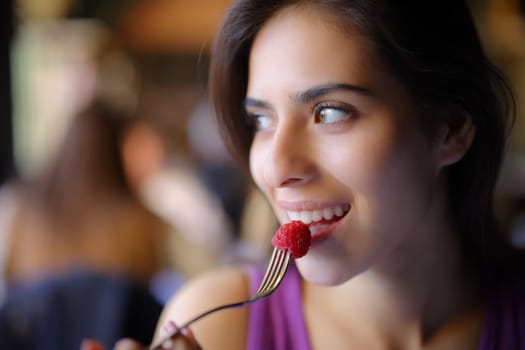 Happy woman eating blackberry looking at side sitting in a restaurant