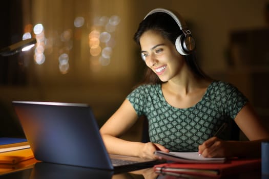 Happy student in the night elearning with laptop and headphone at home
