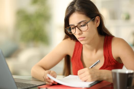 Student wearing glasses taking notes at home