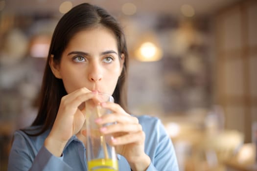 Front view of a distracted woman sipping orange juice with straw in a restaurant