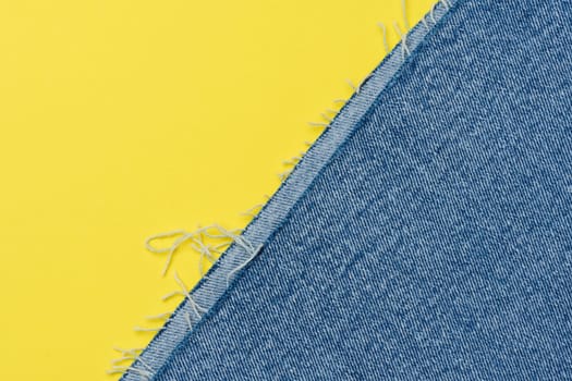 Torn edges of blue jeans on a yellow background