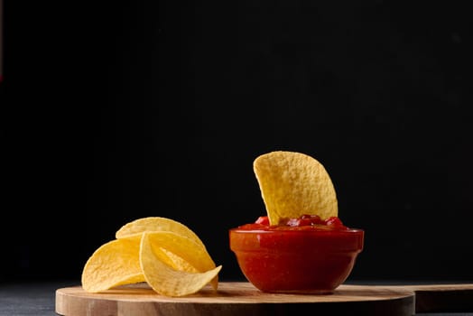 Potato chips in a wooden bowl and a bowl of sauce on a black table, snack