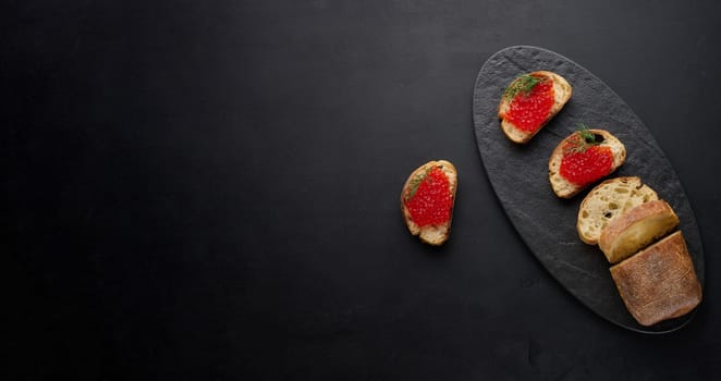 Red caviar on slices of white wheat bread on a black table, concept of luxury and gourmet cuisine. Copy space