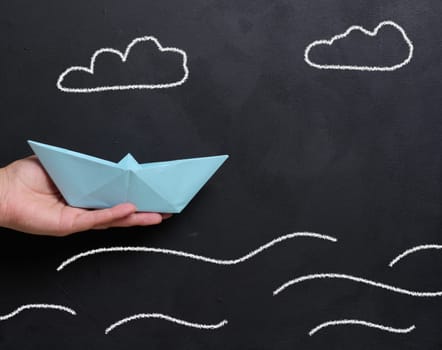 A female hand holds a paper boat against a backdrop of a board with drawn waves, representing the concept of mentorship and support