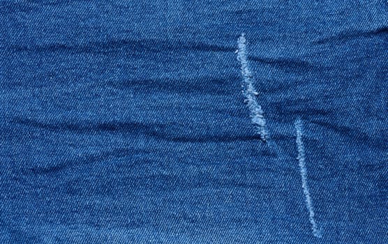 Fragment of blue jeans fabric with a hole, full frame, close up