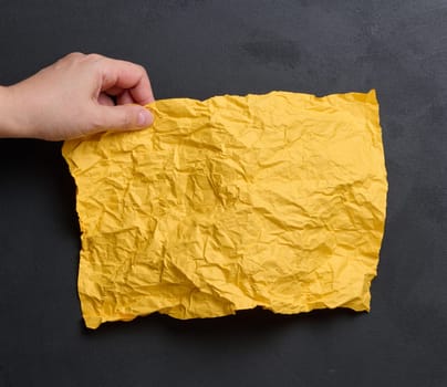 A woman's hand holds a yellow crumpled sheet of paper