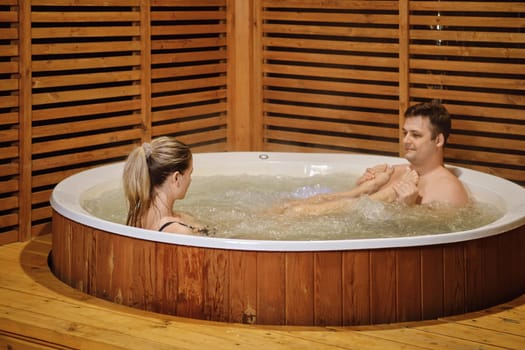 Playful woman put her feet on chest of her husband while relaxing in a jacuzzi in the evening
