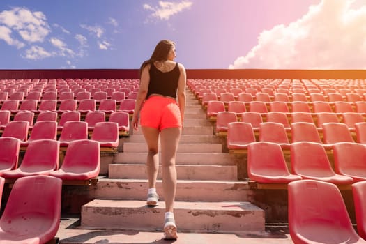 A female coach with dark hair stands on the red running track of the stadium, dressed in sports uniform.