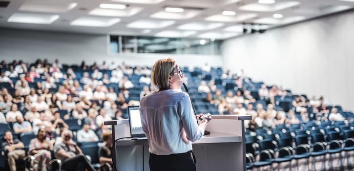 Female speaker giving a talk on corporate business conference. Unrecognizable people in audience at conference hall. Business and Entrepreneurship event