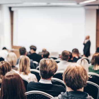 Speaker giving a talk in conference hall at business event. Rear view of unrecognizable people in audience at the conference hall. Business and entrepreneurship concept