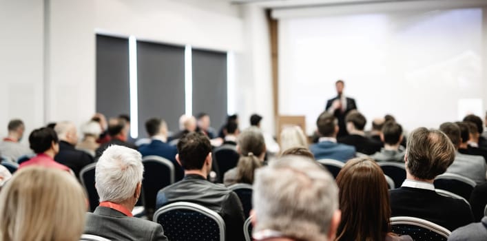 Speaker giving a talk in conference hall at business event. Rear view of unrecognizable people in audience at the conference hall. Business and entrepreneurship concept