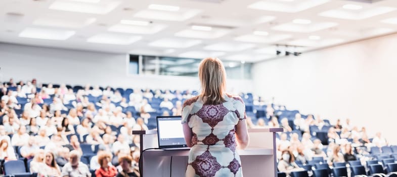 Female speaker giving a talk on corporate business conference. Unrecognizable people in audience at conference hall. Business and Entrepreneurship event.
