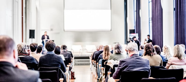 Speaker giving a talk in conference hall at business event. Rear view of unrecognizable people in audience at the conference hall. Business and entrepreneurship concept