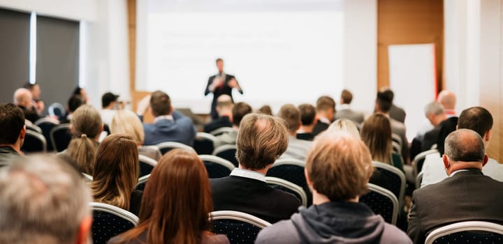 Speaker giving a talk in conference hall at business event. Rear view of unrecognizable people in audience at the conference hall. Business and entrepreneurship concept