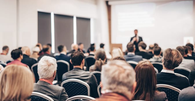 Speaker giving a talk in conference hall at business event. Rear view of unrecognizable people in audience at the conference hall. Business and entrepreneurship concept