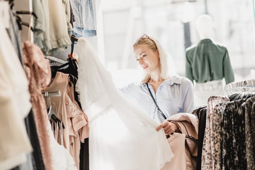 Woman shopping clothes. Female shopper looking at fashionable clothes indoors in clothing store.