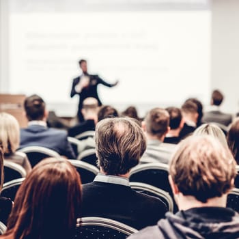 Speaker giving a talk in conference hall at business event. Rear view of unrecognizable people in audience at the conference hall. Business and entrepreneurship concept