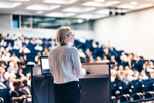 Female speaker giving a talk on corporate business conference. Unrecognizable people in audience at conference hall. Business and Entrepreneurship event