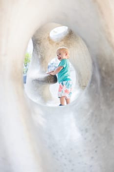 Child playing on outdoor playground. Toddler plays on school or kindergarten yard. Active kid on stone sculpured slide. Healthy summer activity for children. Little boy climbing outdoors