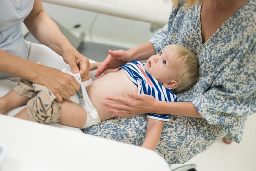 Infant baby boy child being examined by his pediatrician doctor during a standard medical checkup in presence and comfort of his mother. National public health and childs care care koncept