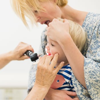 Infant baby boy child being examined by his pediatrician doctor during a standard medical checkup in presence and comfort of his mother. National public health and childs care care koncept