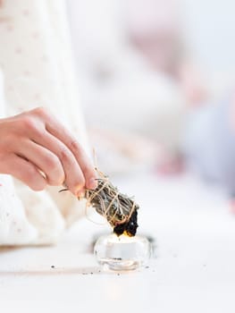 Woman lighting a smudge kit with herbal stick. Natural elements for cleansing environment from negative energy, adding positive vibes. Spriritual wellness practices