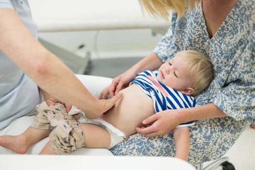 Infant baby boy child being examined by his pediatrician doctor during a standard medical checkup in presence and comfort of his mother. National public health and childs care care koncept