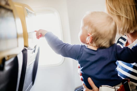 Mom and child flying by plane. Mother holding and playing with her infant baby boy child in her lap during economy comercial flight. Concept photo of air travel with baby. Real people