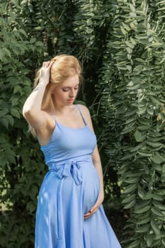 Pregnant beautiful young  woman is posing with hand in her hair outdoors. Horizontally.