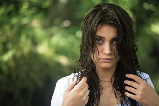 Sad attractive girl is holding her wet hair with both hands looking at the camera closeup. Horizontally.