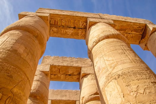 Ancient Egyptian hieroglyphs and symbols carved on columns of the complex of Karnak temple. Tall columns against blue sky. of Karnak. Luxor, Egypt