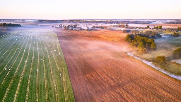 Warm sunny September morning. Autumn beautiful fog landscape. Small river curves in trees. Bright sunny misty riverside. Scenic view of rural sunrise. Village in Agriculture fields. Europe, Belarus
