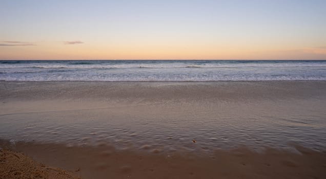 Looking east over the Pacific Ocean, Queensland, as the sun sets in the west, waiting for the full moon to rise above the horizon while the surf waves break on a sandy beach at Kawana, Sunshine Coast, a popular holiday destination.