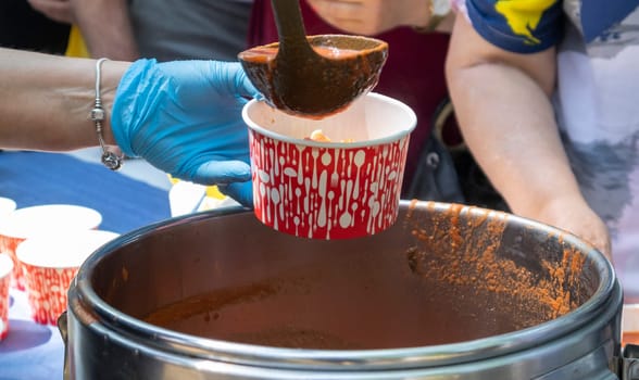 Tomato soup with pasta is a Polish dish. Zupa pomidorowa. Hot soup made from grated tomatoes. People and tourists walk, eat and buy food at the street food festival. Ukraine, Kyiv - August 17, 2023