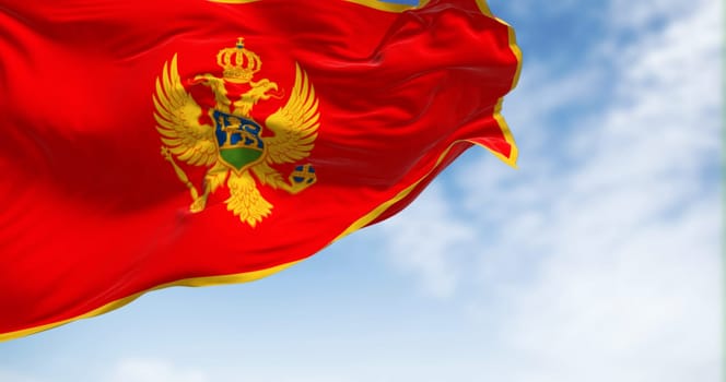 National flag of Montenegro waving in the wind on a clear day. Red with a golden border and features the national coat of arms in its center. 3d illustration render. Selective focus. Fluttering fabric