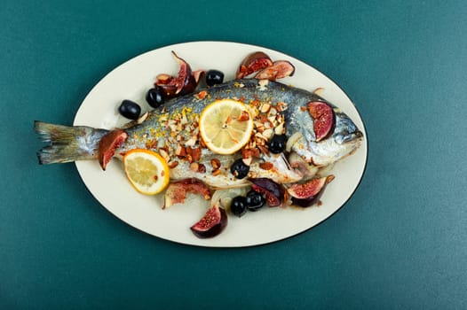 Roasted dorado fish with almonds and figs on a white plate. Autumn recipe.